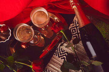 Aesthetics Valentines day background. Seasonal romantic dinner with glasess, bottle of champagne, red roses and chocolate candies flat lay