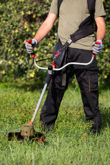 Man mowing the grass at his garden by using string trimmer