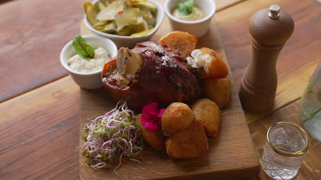Oven-baked pork knuckle served on a wooden board along with source, potatoes and vegetables. Polish cuisine concept. High quality 4k footage