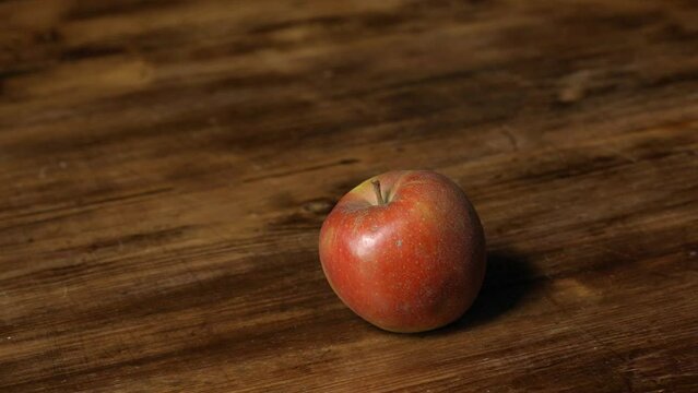 Three Boskoop apples are taken by a man's hand from a wooden table with brown structure in slow motion.