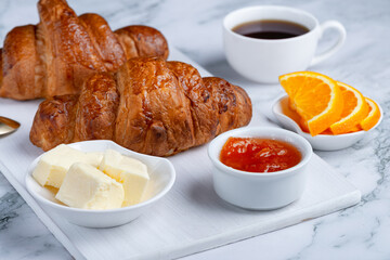 Fresh sweet croissants with butter and apricot jam for breakfast. Continental breakfast on a white concrete table