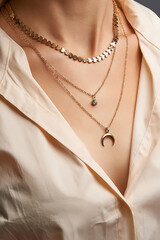Cropped close-up portrait of a woman, demonstrating gold necklaces with pendants in a beige shirt....