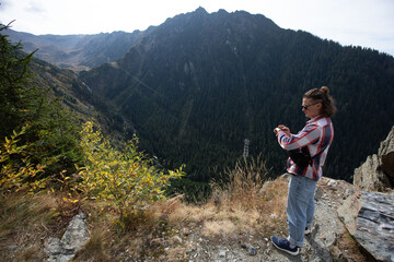 a guy in black glasses, a shirt, jeans and sneakers stands in the mountains near the abyss and looks at the watch on his wrist. a hipster checks his watch in the mountains