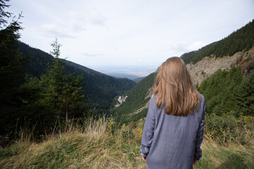 Naklejka na ściany i meble the back of the girl looking at the green mountains. a woman with loose hair stands in the mountains.