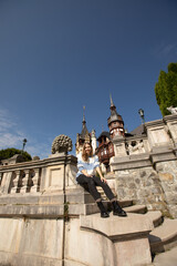 a beautiful girl in a sweater and black jeans sits on the stairs near Peles Castle in Romania. tourism.