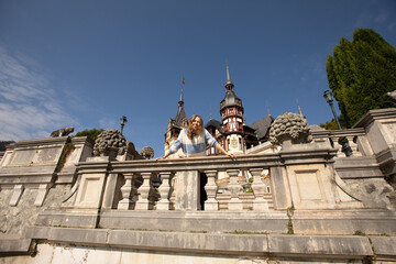 Obraz premium beautiful tourist girl put her hands on the concrete railing near Peles Castle in Romania. a tourist in an ancient fortress. summer