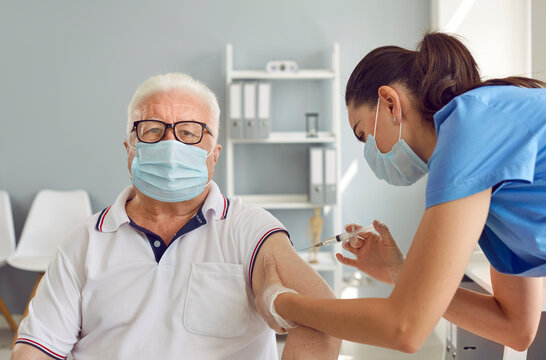 Senior man in medical protective mask receives vaccination against COVID-19 at vaccination center. Young nurse makes injection in hand of old man. Concept of vaccination for older people.