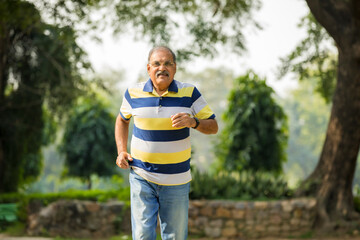 Indian old man running or jogging at park