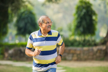 Indian old man running or jogging at park