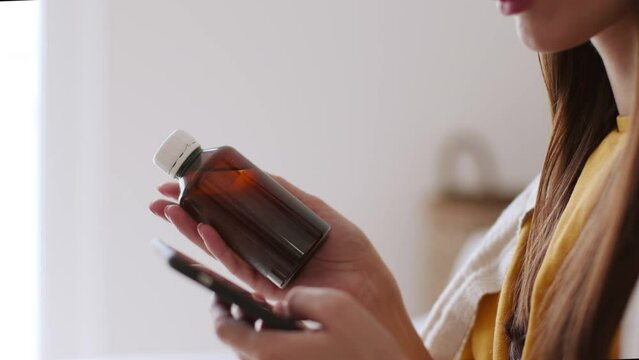 Online medical help. Unrecognizable sick woman holding bottle of syrup and typing on smartphone, chatting with doctor