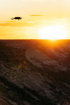 Silhouette of a drone flying towards golden lights of setting sun behind big cliffs in desert area