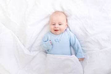 laughing baby boy on the bed under the blanket, healthy sleep baby