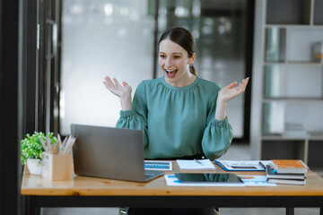 Business woman very happy and excited doing winner gesture with arms raised at table office, Business success and celebration concept.