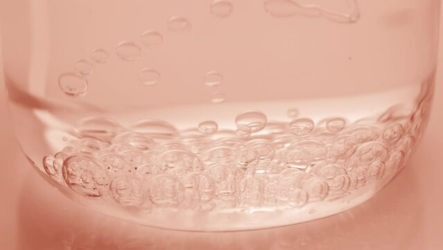 Side view extreme close-up shot of transparent bubbles sink to the bottom of beaker with water on beige background | Abstract skincare cosmetics with lactic acid formulation concept