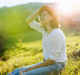 Happy pretty young cheerful woman in white shirt enjoying sunny day while sitting on the green...