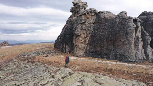 Hiker with backpack trekking poles sticks walking on hilly mountain with rock stone towers of buttes. Travel and tourism in national park. Aerial view following tourist. Hiking exploring places earth