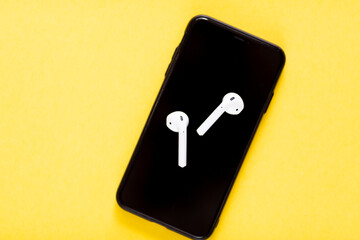 Flat lay with smartphone and wireless headphones on yellow background with copy space