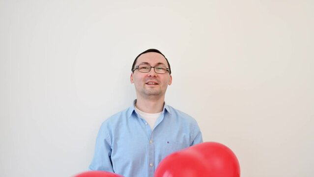 Happy man in glasses plays with heart balloons. Valentines day,anniversary,birthday concept	