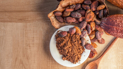 Cocoa powder and cocoa beans with cocoa pods on wooden background.