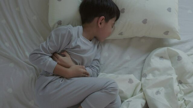 Top View of Asian boy lying in bed with stomach ache