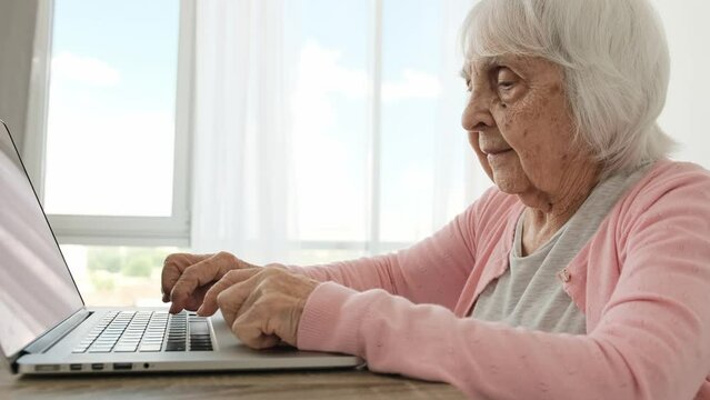 Senior woman typing on laptop keyboard. slowly at home. Elderly female person pushing notebook buttons and looking at screen