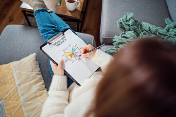 Top view relaxed young woman drawing work-life balance wheel sitting on the sofa at home. Self-reflection and life planning. Coaching tools. Finding Balance in Your Life. Selective focus.