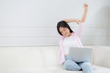 Beautiful young asian businesswoman sitting on sofa and working from home and break while stretch arm for relax in living room at home, woman is freelance working on laptop computer, business concept.