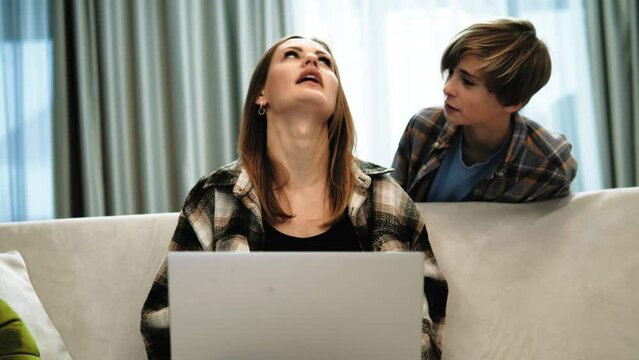 Annoying irritated freelancer woman trying to work on laptop while her naughty teenager son distracting, asking questions. Bad behavior of teenage boy at home. Parent problem. Distractions at work