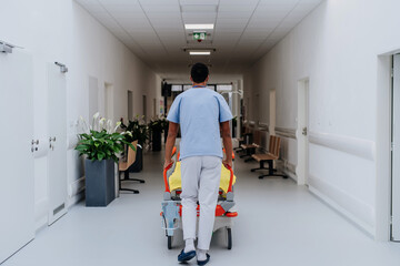 Fototapeta na wymiar Rear view of caregiver pushing hospital bed at corridor.
