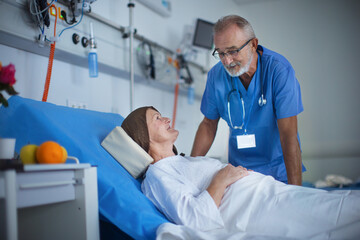 Elderly doctor examining patient in hospital room, talking with her.