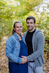 Portrait of happy pregnant woman and her husband, standing in forest.