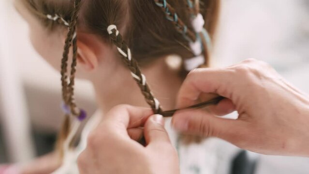 Barber braiding pigtail hairstyle for child girl in salon. Hairdresser hands and kid face during trendy hair weaving closeup