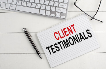CLIENT TESTIMONIALS text on notebook with keyboard , pen glasses on white wooden background