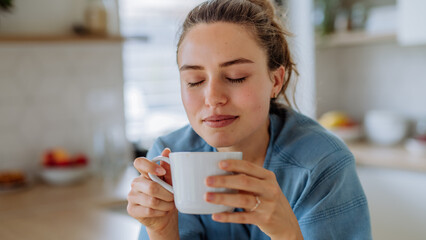 Young woman enjoying cup of coffee at morning, in her kitchen. - Powered by Adobe