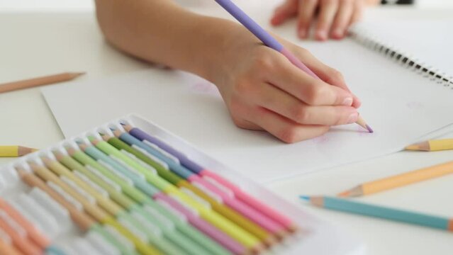 Child hand drawing with crayons from coloful palette on white paper. Person kid painting with pencils in album