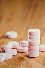 Fototapeta na wymiar Drugs ballance concept. The tower of small pink pills on wooden background with plenty of tablets around.