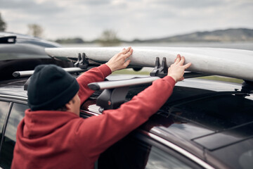 Windsurfer and camper unpacking equipment from a car in nature near the lake shore.