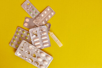 Packets with various pills and a container with liquid on a yellow background.