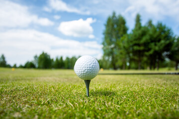 Golf ball on the stand in the green grass against the background of the sky with clouds. High quality photo