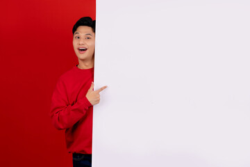 Handsome asian man wearing red casual clothes with hand pointing blank announcement banner in red...