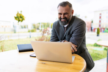 mature male businessman working on laptop smiling outside