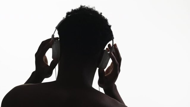 Music chill. Sound technology. Back view silhouette of unrecognizable relaxed man in headphones enjoying listening to audio dancing isolated on white free space background.