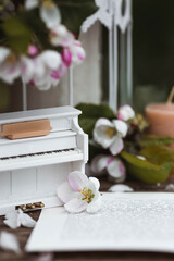 A beautiful postcard. A white piano, a statuette, candles, a book and a vase with a bouquet of blooming apple trees. A beautiful still life. The concept of classical music, poetry.