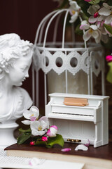 Fototapeta na wymiar A beautiful postcard. A white piano, a statuette, candles, a book and a vase with a bouquet of blooming apple trees. A beautiful still life. The concept of classical music, poetry.