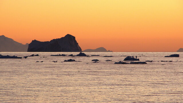 Iceberg silhouetted against an orange sky at sunset at Cierva Cove, Antarctica