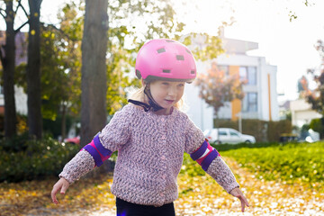 Smiling child girl in a helmet in protection rollerblades in the park