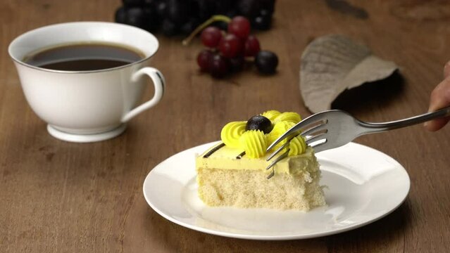 Eating delicious homemade sponge cake in white ceramic dish with hot black coffee in white ceramic cup and fresh ripe organic grapes.