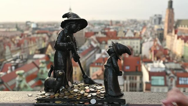 Tourist hand put coins to famous dwarf gnome sculpture in Wroclaw, Poland with city view. Money tradition and monument in Europe Union country