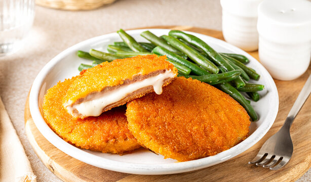 Plate with fried chicken Cordon bleu with melted cheese and ham, in breadcrumbs, green beans and lemon.