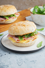 Two homemade sandwiches with ham, cheese and arugula on a concrete table.